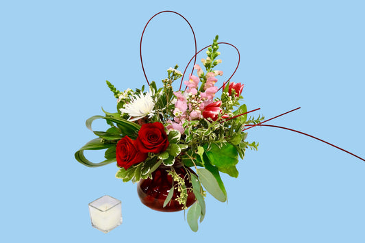 Floral arrangement with red and pink flowers in a clear vase on a white surface.