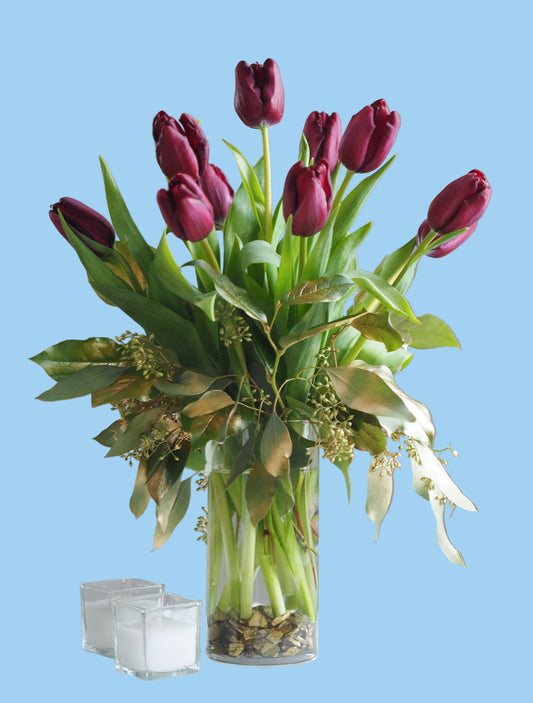 Bouquet of purple tulips in a clear vase on a white surface with a gray background
