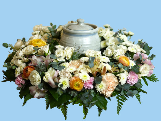 Floral arrangement surrounding a urn on a white background